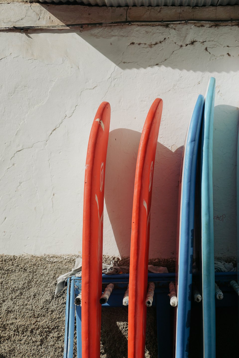 Orange and blue surfboards stand upright against a white wall.