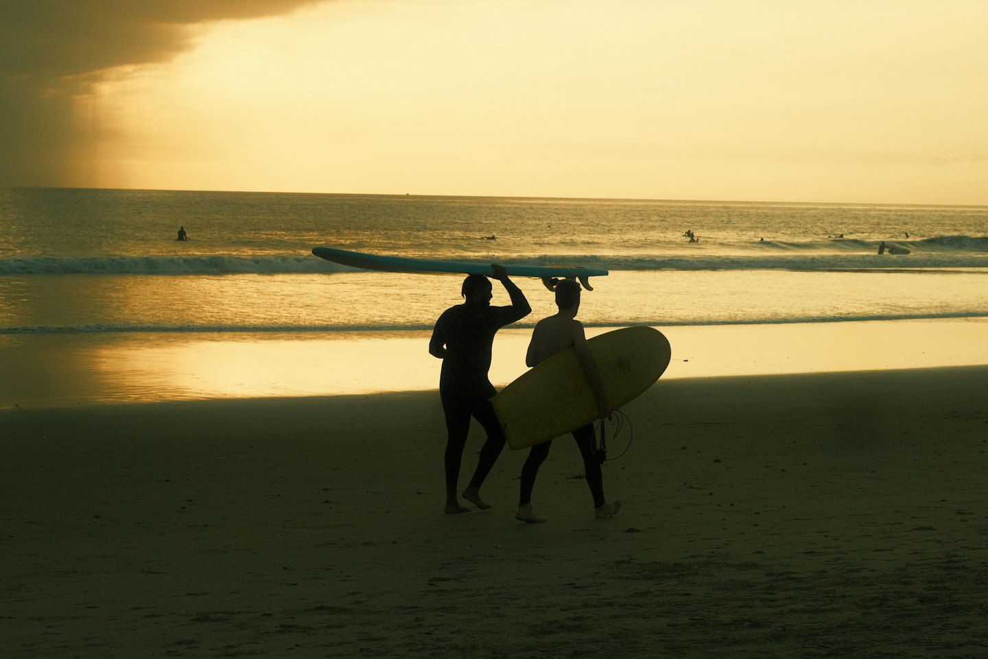 Two surfers walk across the sand towards the ocean.